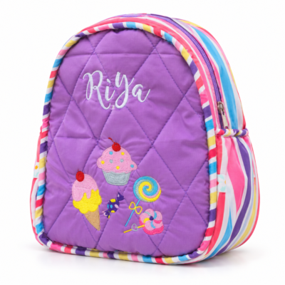 Purple quilted kids' backpack with colorful striped trim and embroidered cupcakes and lollipops, plus the name 'Riya'