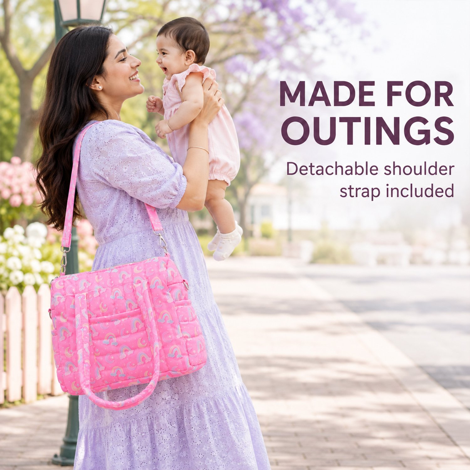 Mother in a lavender dress lifts a smiling baby outdoors; a pink rainbow-patterned bag hangs from her shoulder (advertisement).