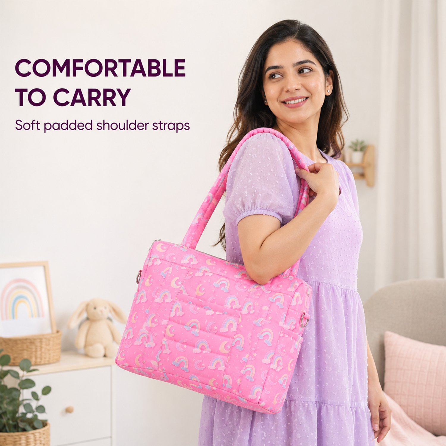 Smiling woman in a lavender dress carries a pink quilted shoulder bag with a rainbow pattern in a cozy room setting.