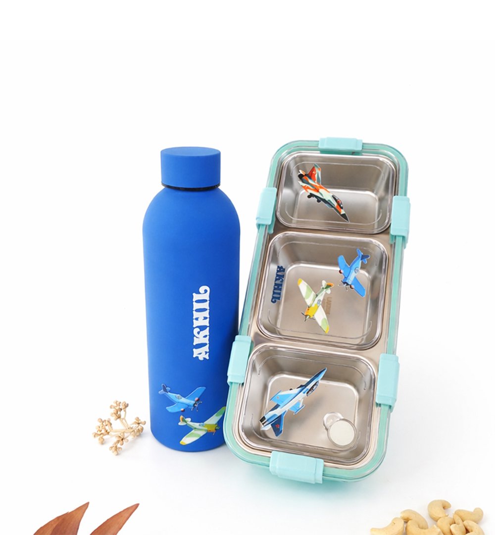 Blue water bottle stands next to a teal, three-compartment lunchbox with airplane stickers on the metal trays.