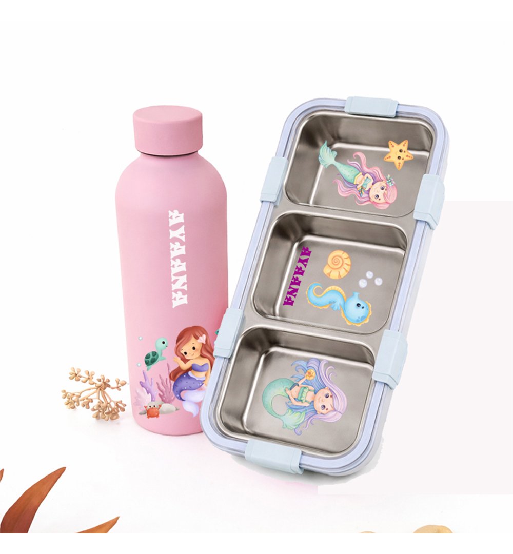 Pink stainless water bottle with mermaid illustration beside a three-compartment metal lunchbox with mermaid decals.