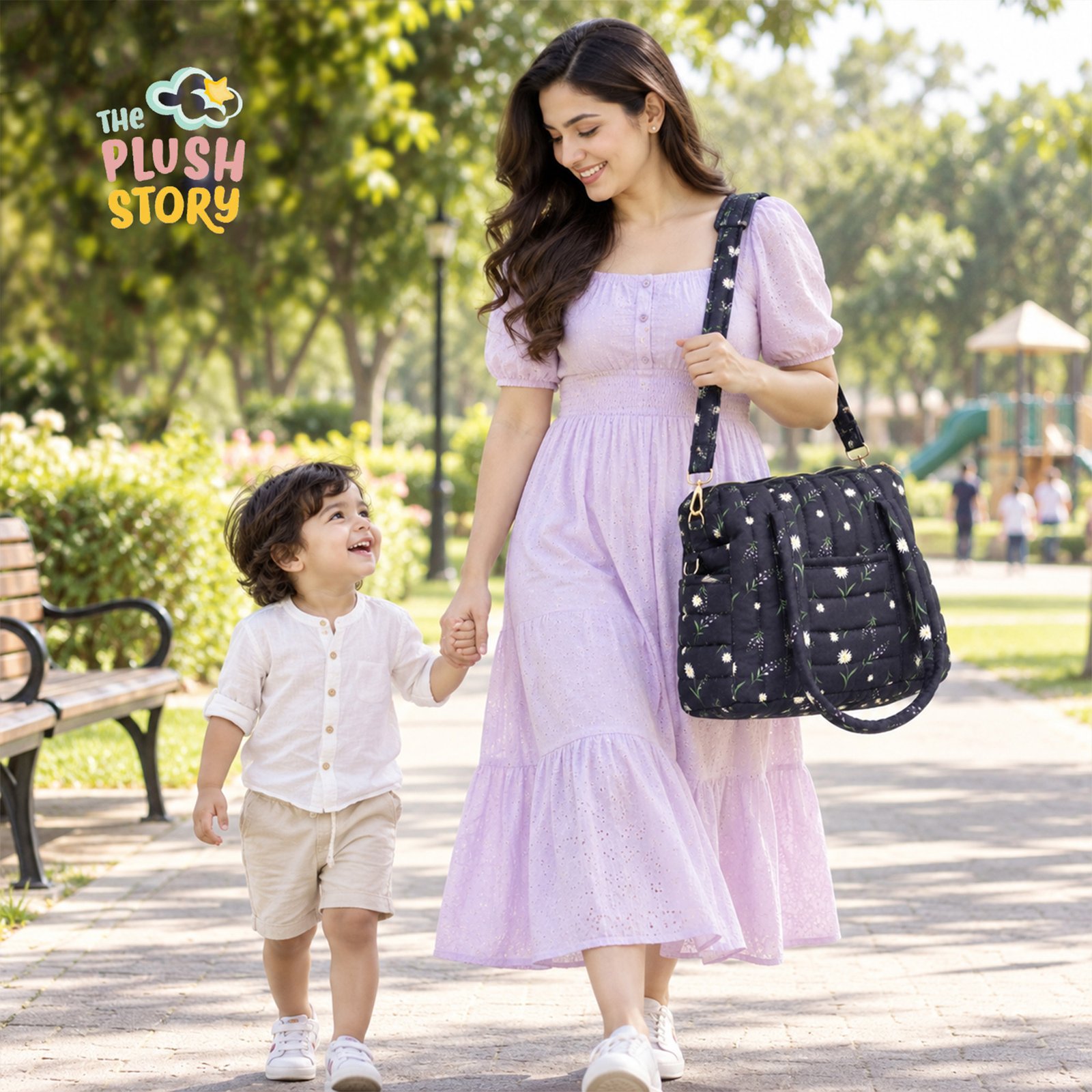 Woman in a lavender dress walks in a sunny park, holding a child’s hand; a large black quilted shoulder bag with white daisies hangs from her side.