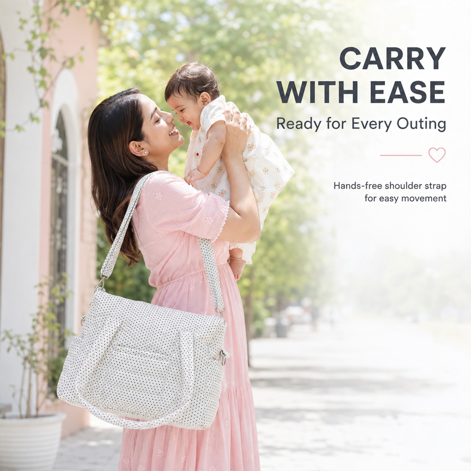 Mother outdoors, smiling as she lifts a baby in a light pink dress with a white polka-dot bag nearby (promo banner)