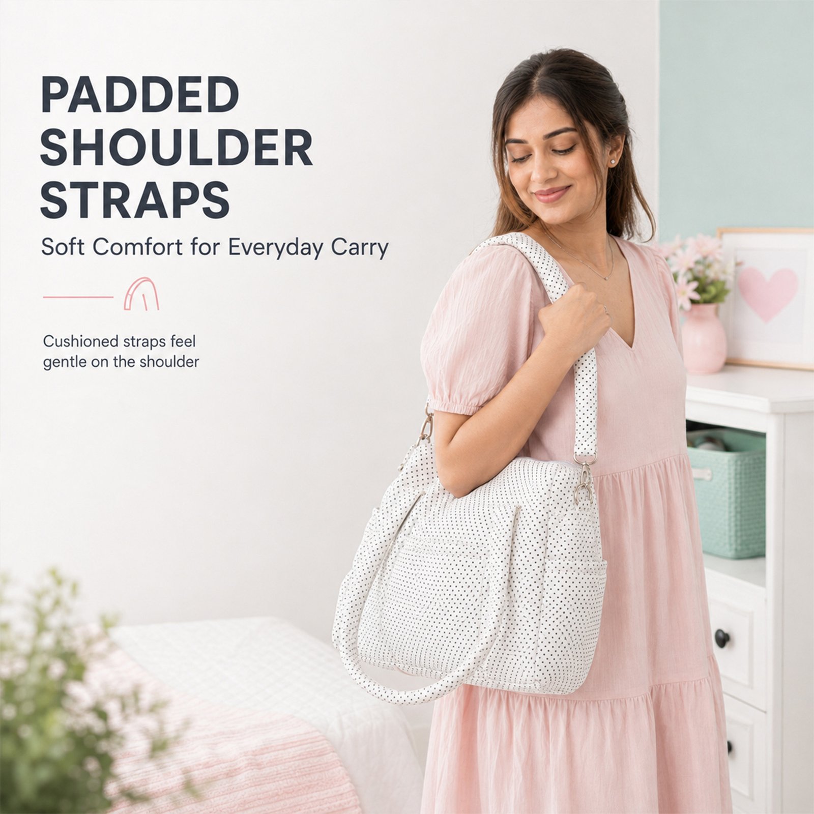 Woman modeling a pink dress with a white polka-dot bag over her shoulder in a pastel bedroom, highlighting padded shoulder straps for everyday use.