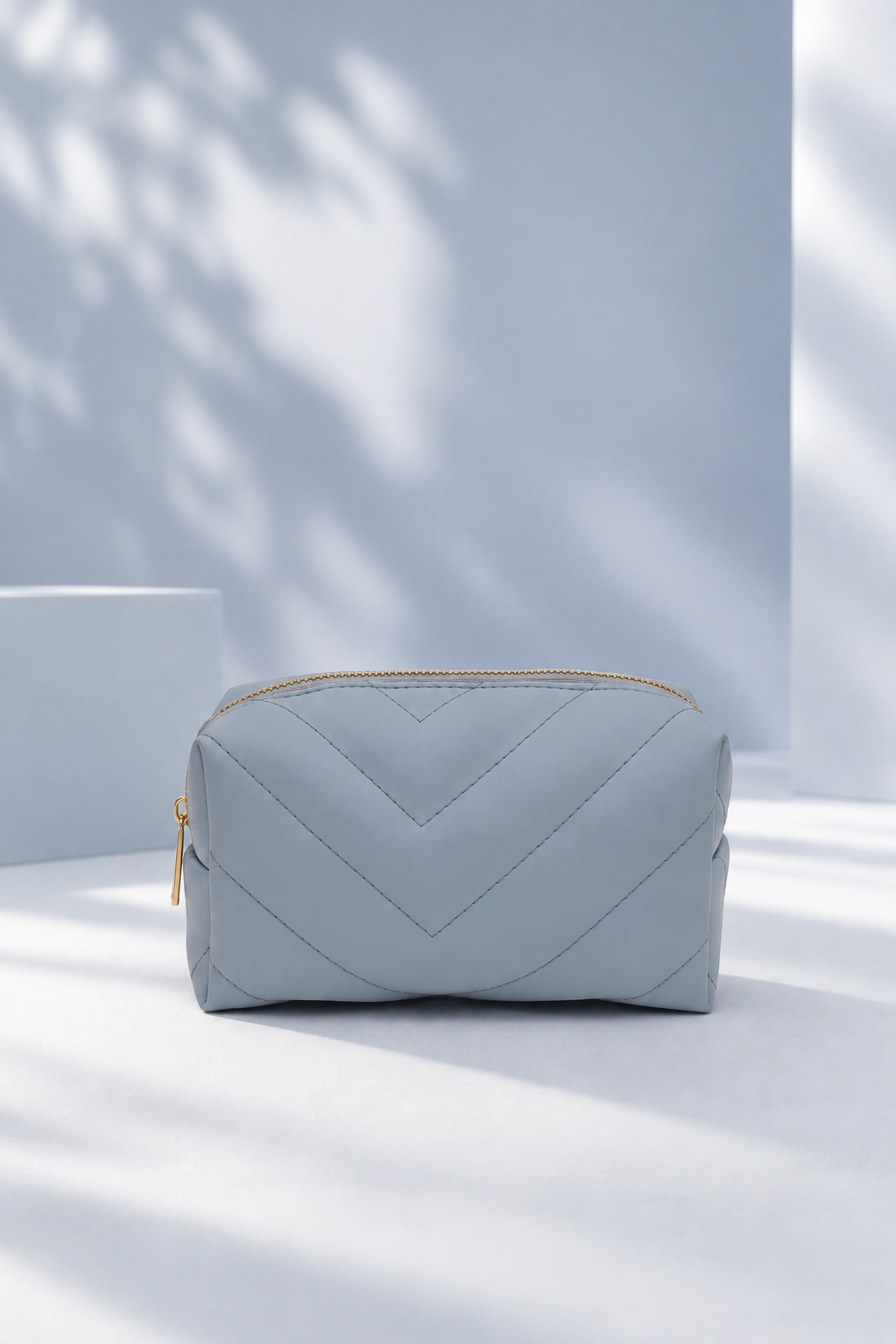 Light blue quilted cosmetic bag with a gold zipper on a pale blue backdrop.