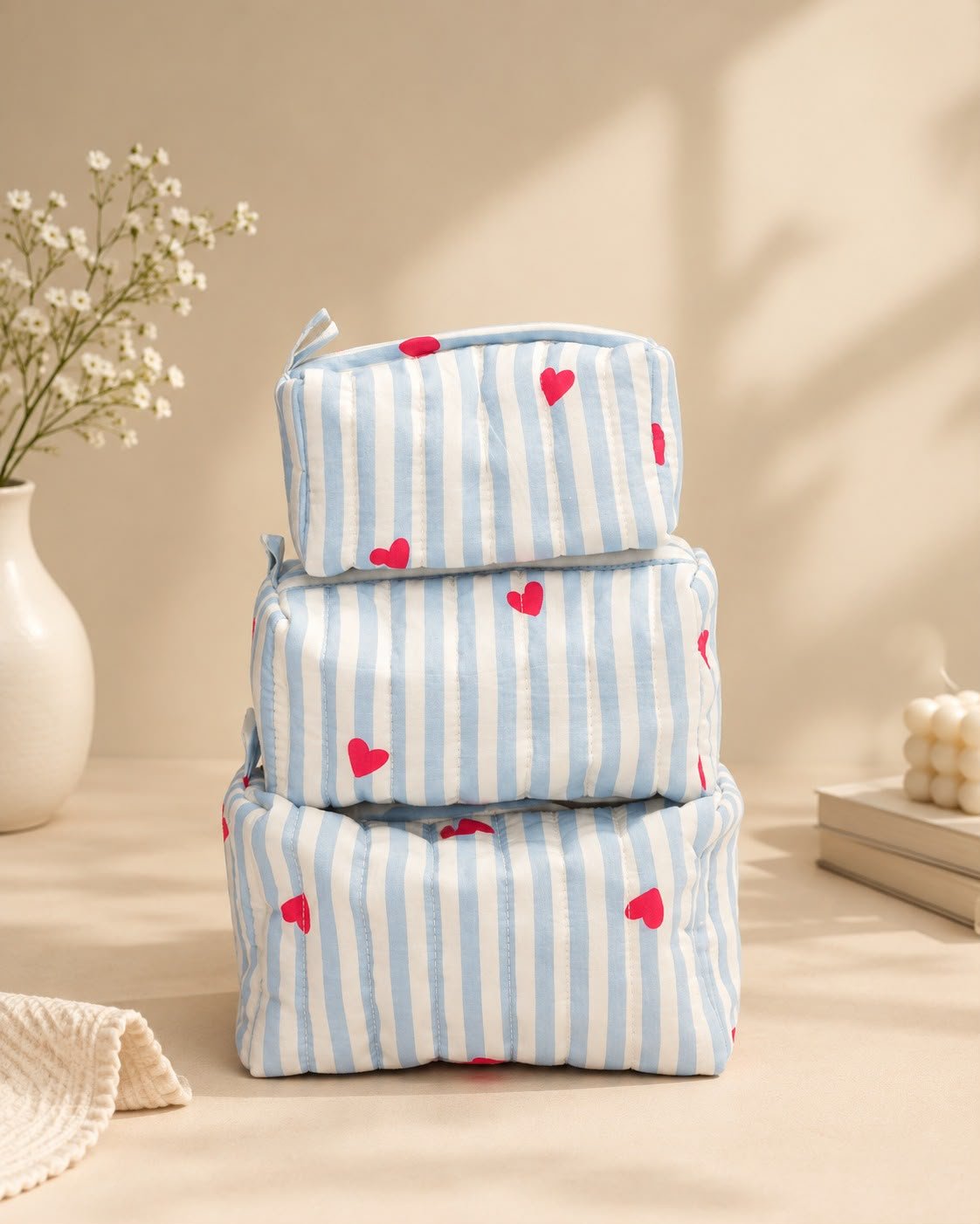 Three blue-and-white striped fabric gift bags with red heart prints stacked on a neutral surface.